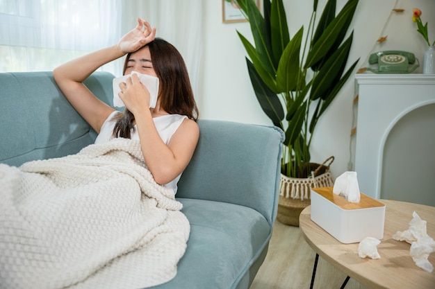 Photo sick female sitting under blanket on sofa and sneeze with tissue paper in living room
