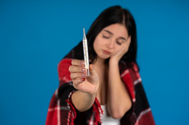 Photo sick girl in checkered blanket holding thermometer isolated on blue