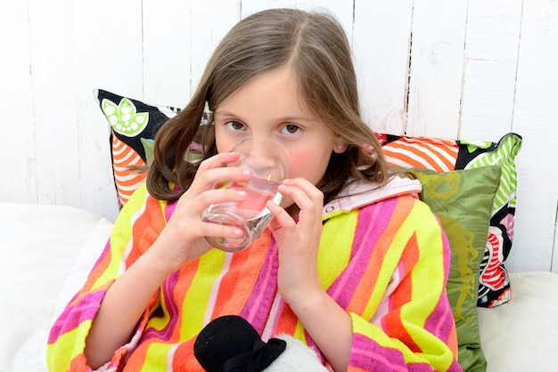 Una ragazza malata che beve un bicchiere d'acqua