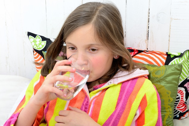 Una ragazza malata che beve un bicchiere d'acqua