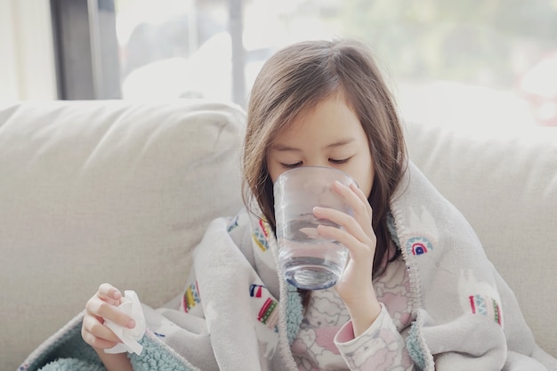 sick girl drinking water on sofa at home