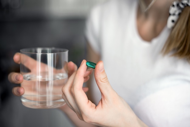 Foto la ragazza malata beve una pillola fredda che guarisce e non fa più male, e beve acqua da una tavoletta di vetro a casa