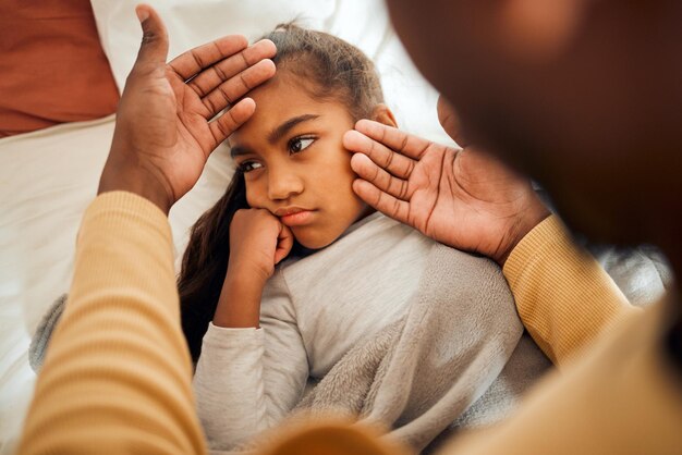 Sick girl and father checking high temperature with hands on ill kid or daughter lying on a bed feeling sad concern care and parent in bedroom with worried child with flu cold or fever