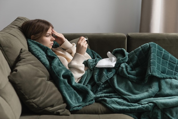 A sick girl lies on the bed and holds her head sees an increased temperature on the thermometer