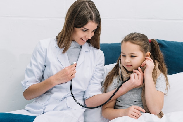 Photo sick girl listening the heart beat of smiling female doctor with stethoscope