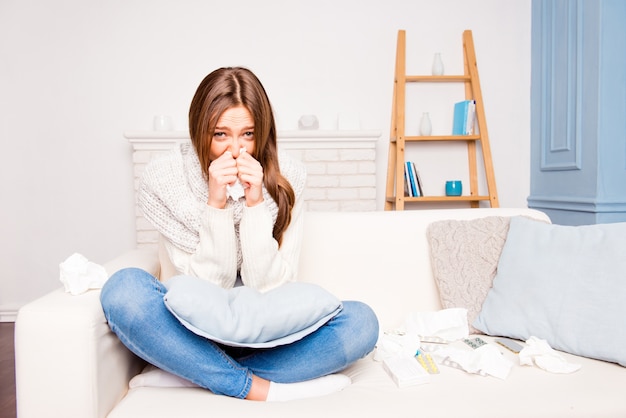 Sick  girl with fever sneezing in tissue sitting on sofa