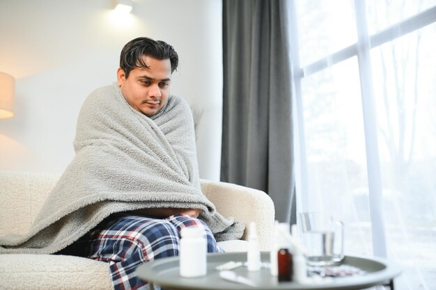 Sick Indian man in plaid sit alone shivering from cold Unhealthy Arabian guy sit on chair feeling discomfort try to warming up