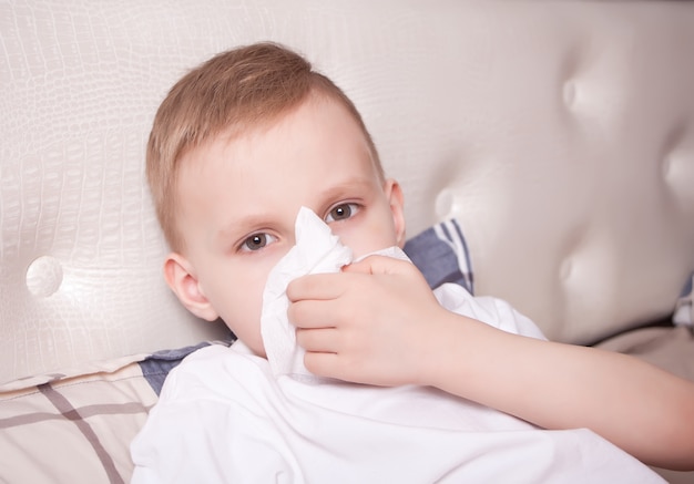 Sick little blond boy blowing her nose