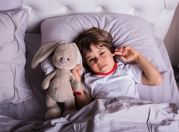 Больной мальчик в пижаме лежит в постели с мягкой игрушкой
