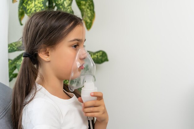 sick little girl makes inhalation over grey background with copy space. Girl making inhalation with nebulizer at home. child asthma inhaler inhalation nebulizer steam sick cough.