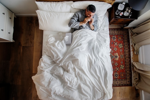 Photo sick man on the bed blowing his nose