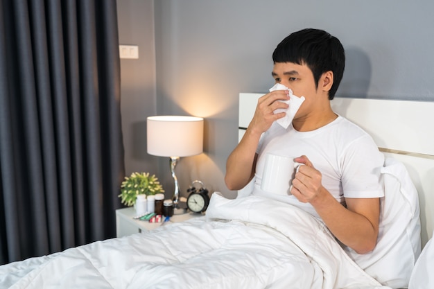 Sick man drinking a cup of hot water on bed