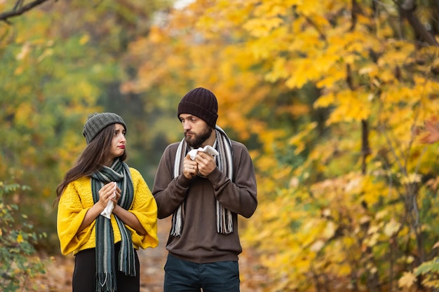 Sick man and girl sneeze and blow their nose in autumn in the park.