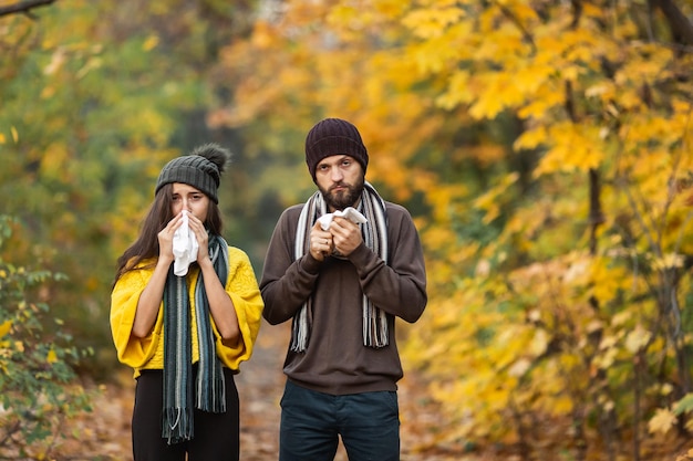 Sick man and girl sneeze and blow their nose in autumn in the park