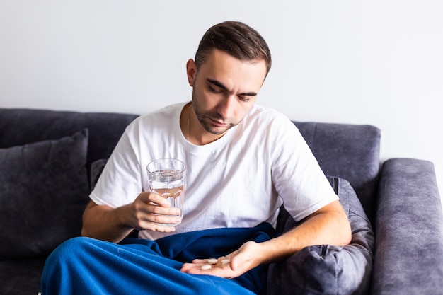 Sick man holding pills and water lying on the sofa