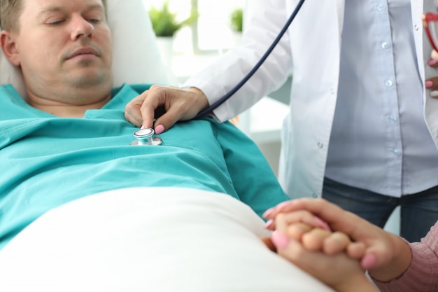 Sick man lies on bed in clinic, doctor examines