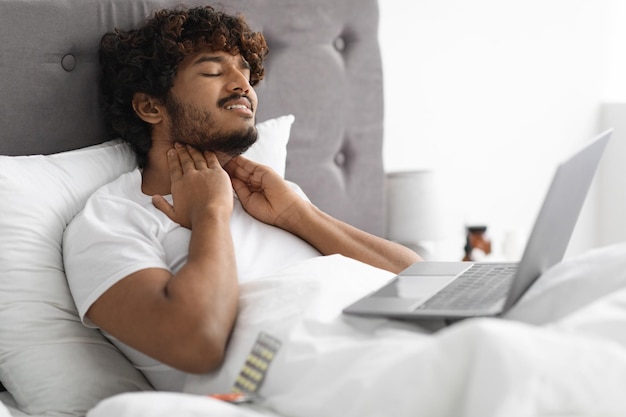 Sick man sitting in bed calling doctor by laptop
