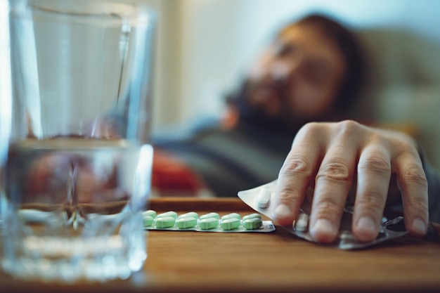 Photo sick man staying in bed taking a pill closeup view of hand