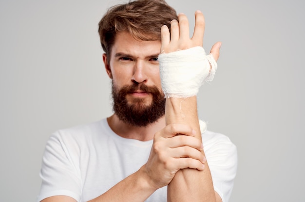 Sick man in a white tshirt with a bandaged hand posing isolated\
background