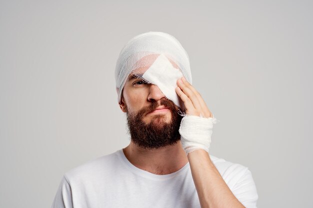 Uomo malato con la testa fasciata e lo sfondo chiaro di ospedalizzazione degli occhi