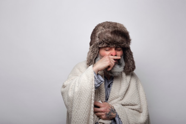 Sick man with cap and blanket covering his nose when sneezing