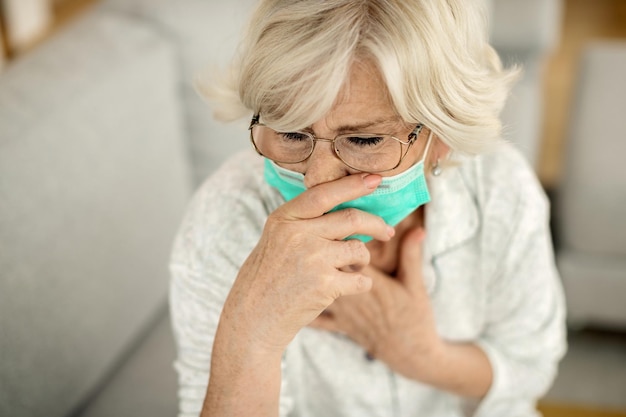 Sick mature woman with face mask coughing at home