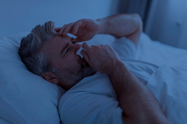 Foto uomo di mezza età malato che starnutisce a letto di notte