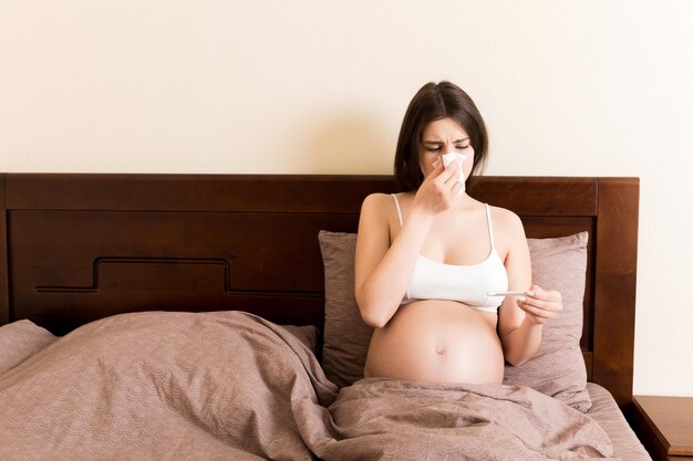 Sick pregnant woman blowing nose into tissue at home Healthy millennial healthcare concept