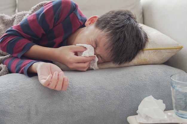Больной предподростковый мальчик чихает, лежа на диване дома
