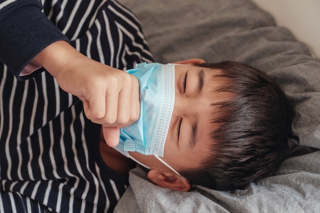 Sick preteen boy wearing a mask and coughing in bed