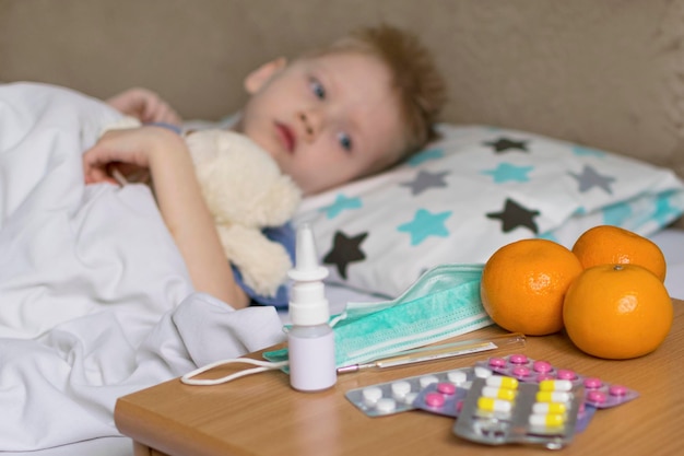 A sick sad child with a temperature and a headache lies in bed next to medication Flu colds disease virus