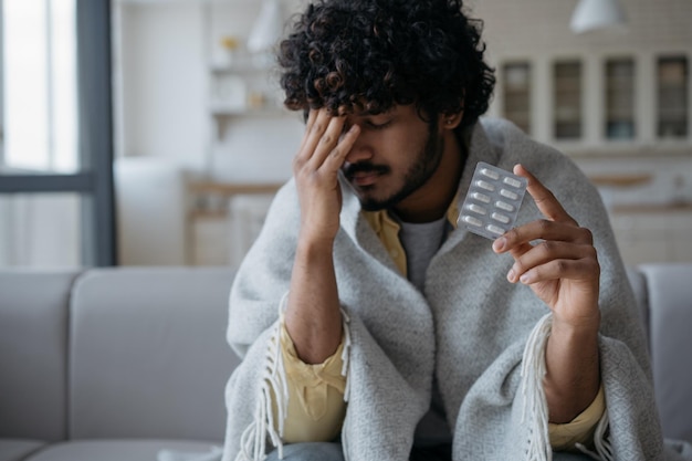 Photo sick sad indian man holding capsule pills having headache at home medicine health care treatment