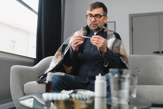 Sick senior man using thermometer checking his temperature suffering from seasonal flu or cold