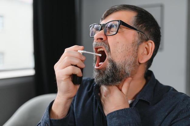 Sick senior man using throat spray at home