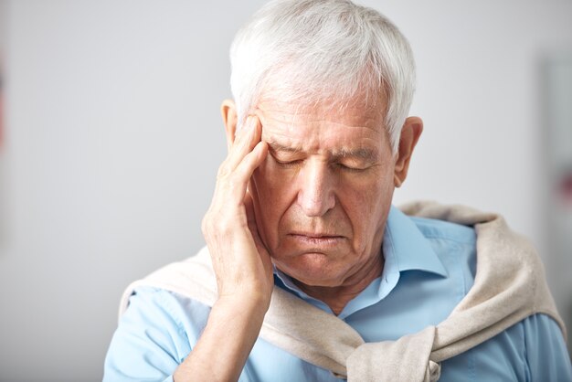 頭痛や倦怠感を表現しながら頭に触れる白髪と目を閉じた病気の年配の男性