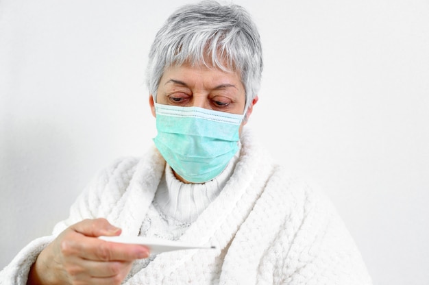 Sick senior woman holding thermometer sit on bed.