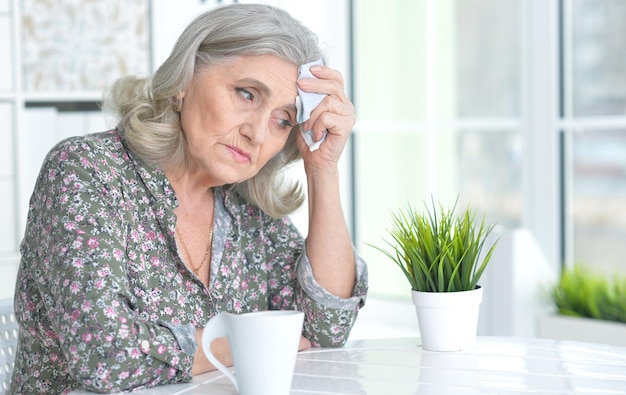 Sick senior woman sitting at table and posing at home