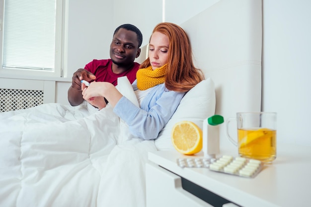 Sick together. Young latin hispanic man and redhaired ginger woman sneezing into paper napkins in bed .