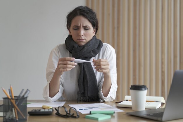 Sick unhealthy italian woman office worker looking at thermometer at work