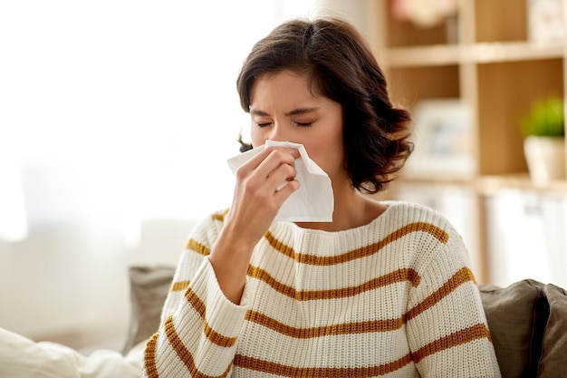 Фото Больная женщина выдыхает нос в бумажной салфетке дома.