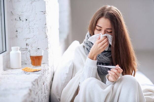 病気の女性が風邪をひいた、病気を感じ、紙拭きでくしゃみをする