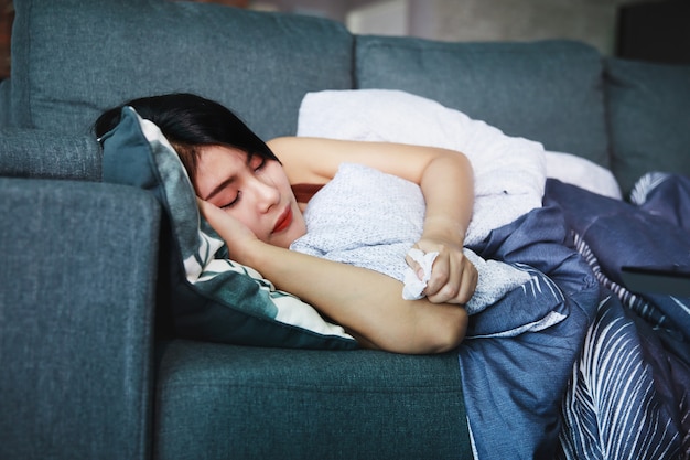 Sick woman covered with a blanket lying on the sofa