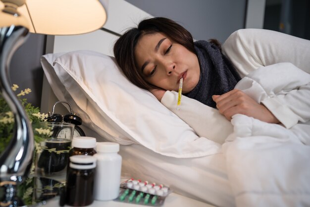 Photo sick woman feeling cold and using thermometer to checking her temperature in bed