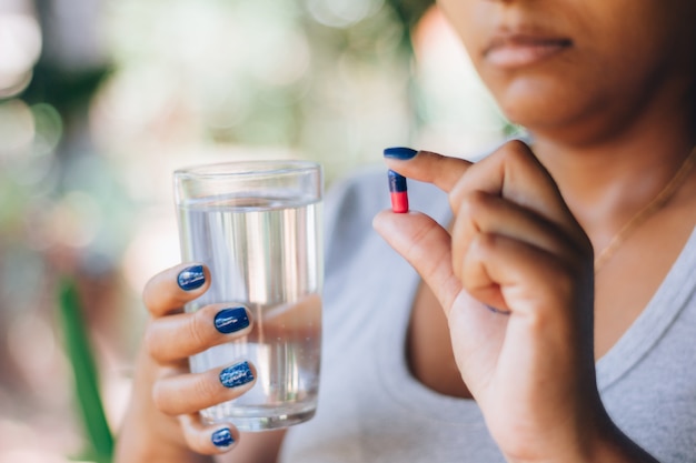 薬の錠剤と水のガラスを保持している病気の女性。薬を飲んでいます。人とセルフメディケーションの概念。健康治療。うつ病、不眠症、痛み