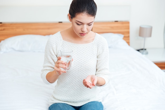 写真 自宅のベッドでピルと水とガラスを保持している病気の女性