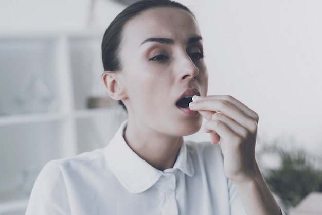 Sick woman holds a pill in her hand in office.