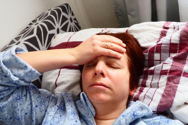 Фото Больная женщина в постели головная боль насморк и насморк бледность лица и дурнота тела плохое самочувствие больной держится рукой за лоб и прикрывает глаза