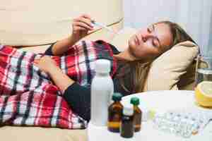 Photo sick woman lying on sofa under wool blanket and looking at thermometer