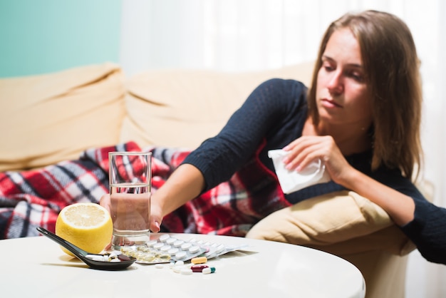 Sick woman lying on sofa under wool blanket sneezing and wiping nose. Caught cold