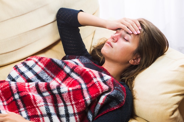 Sick woman lying on sofa under wool blanket